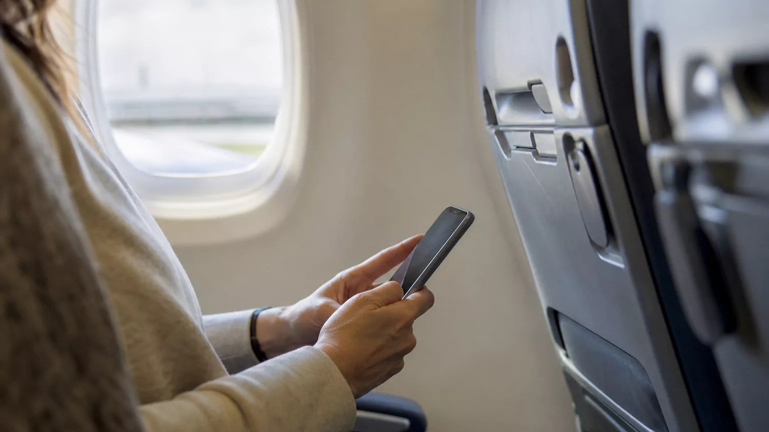 Un passager utilise son téléphone près du hublot dans une cabine d’avion.